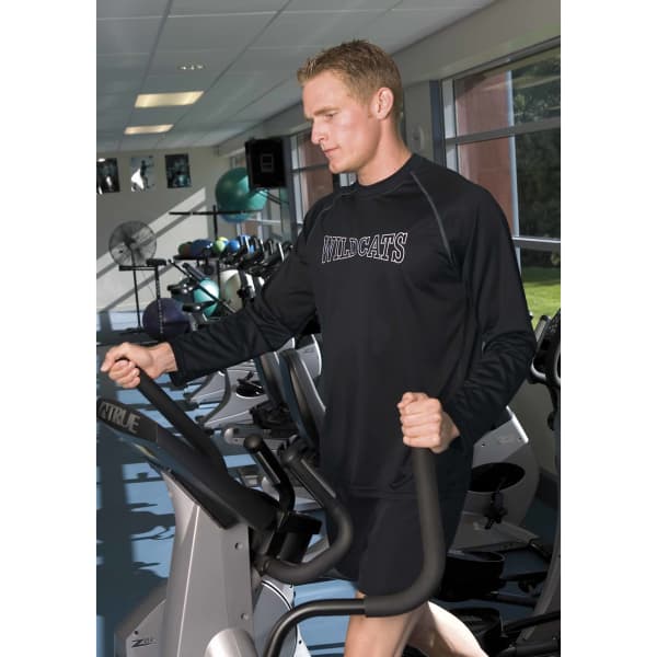 A man is exercising on an elliptical machine wearing a long-sleeve black Dri Gear T-shirt. The shirt features a logo.
