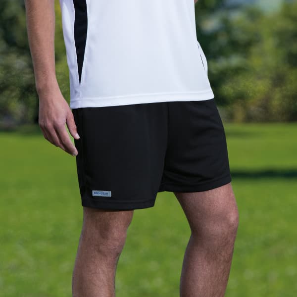 A pair of black sports shorts with a logo, featured against a green outdoor background.