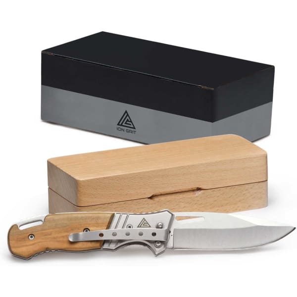 A pocket knife with a stainless steel blade and wooden handle beside a wooden box, with a branded black box in the background.