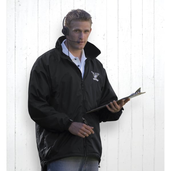 A man wearing a black rain jacket holds a clipboard and pen, with a headset on. The jacket features a logo.