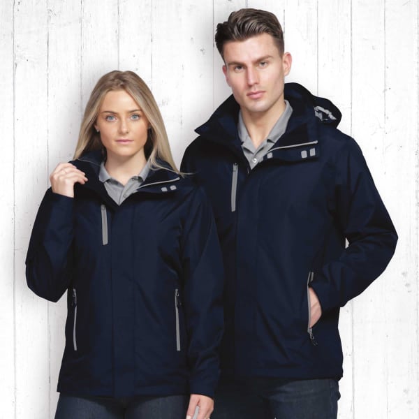 A navy soft shell jacket worn by a man and a woman, featuring zippered pockets and a hood. Both models are posed against a wooden background.