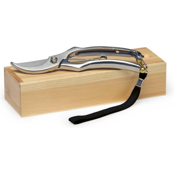 A pair of silver secateurs resting on a wooden block, featuring a black strap.