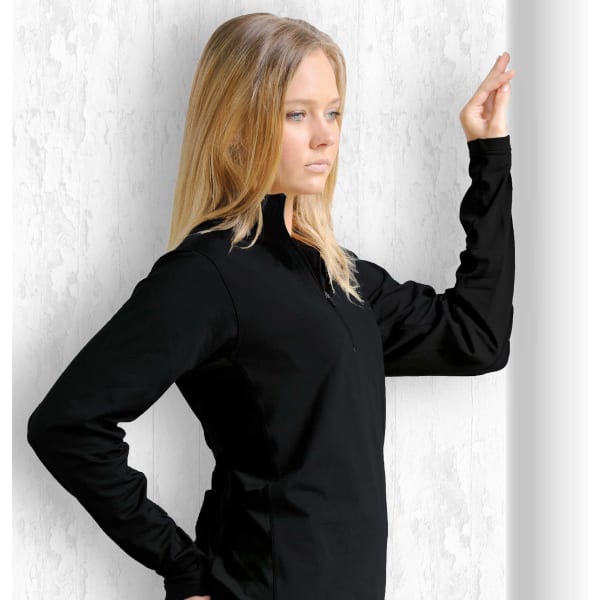 A woman is wearing a black transition top, featuring a zip collar and long sleeves, posed against a textured background.