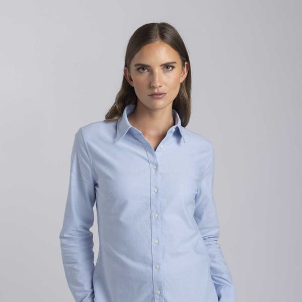 A light blue women's button-up shirt with a collar and long sleeves, featuring branding.