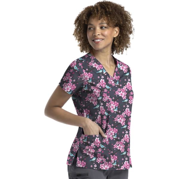 A floral printed curved V-neck top in black, featuring pink blossoms, with a pocket and a model wearing it.