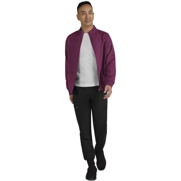 A man models a burgundy jacket with a white shirt and black pants. The jacket features a logo on the chest area.