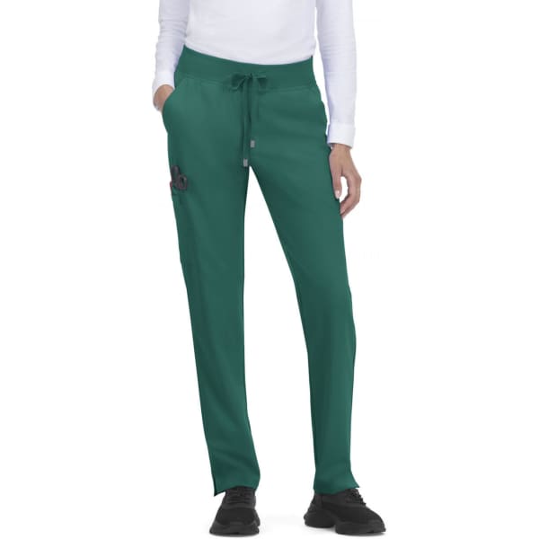 Atria Pant in dark green with pockets and a drawstring waist, worn by a model. Features a small logo.