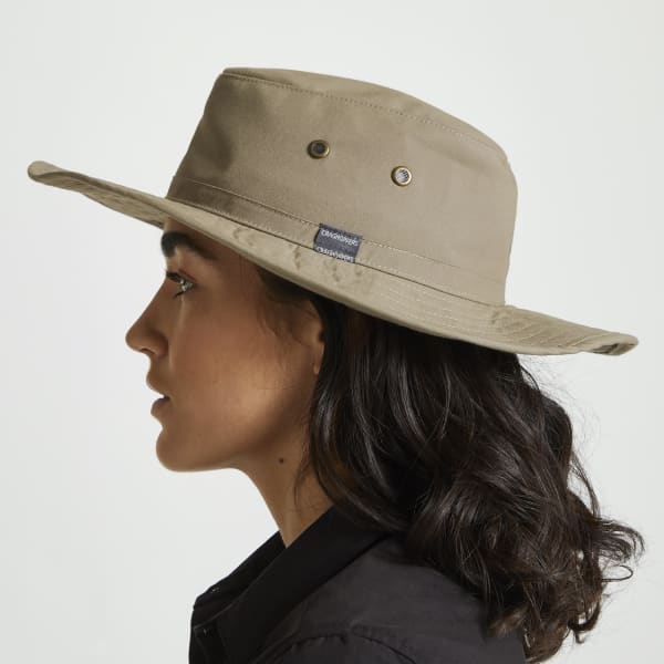 A beige bucket hat with a wide brim, featuring a logo and metal eyelets, worn by a person with medium-length hair.