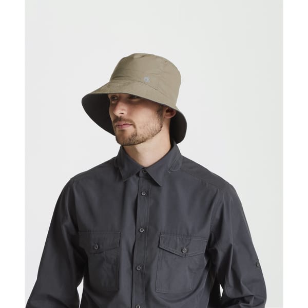 A khaki reversible sun hat worn by a person, featuring a wide brim and a logo on the side.