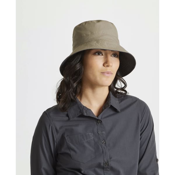 A reversible bucket hat in beige worn by a woman, featuring a wide brim and a simple logo.