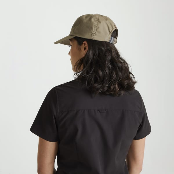 A khaki trucker cap is worn backwards by a person with dark, wavy hair, set against a plain background.