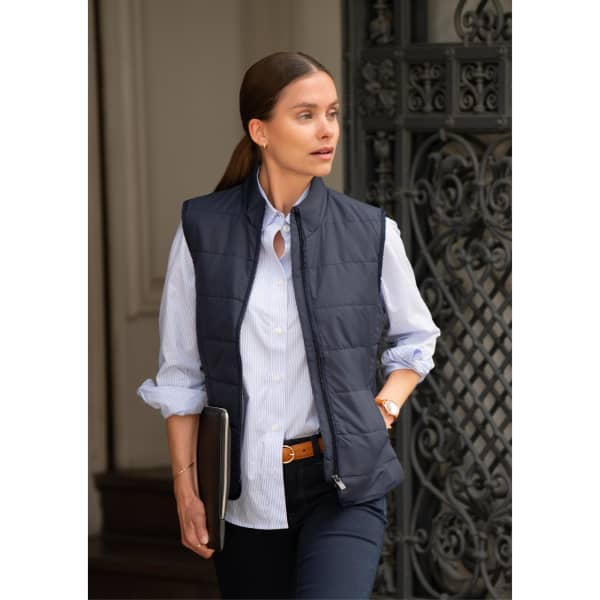 A navy women's vest is worn over a light blue shirt, paired with dark pants and a belt. A logo is visible on the vest.