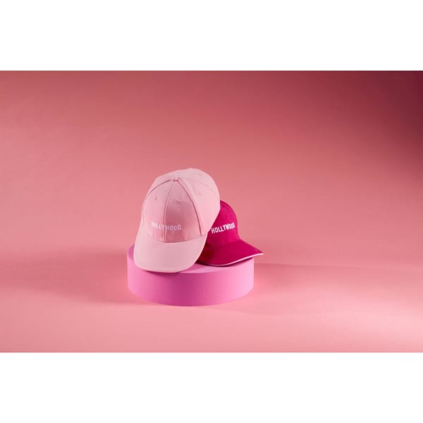 A pink and a magenta 6 Panel Sandwich Cap are displayed against a pink background, with a logo on each cap.