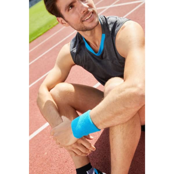 A close-up of a man wearing a blue Terry Wristband on a running track, seated and smiling. He’s in athletic wear.