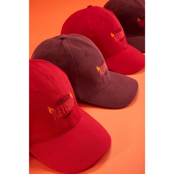 A collection of red and dark grey 6 panel caps with branding, displayed on an orange background.
