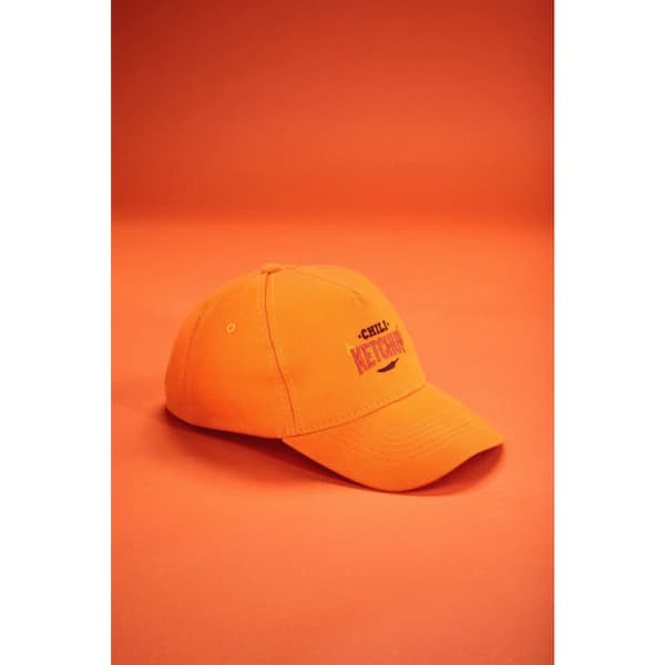 An orange 5 panel cap made from heavy cotton with a logo on the front, set against a similar orange background.
