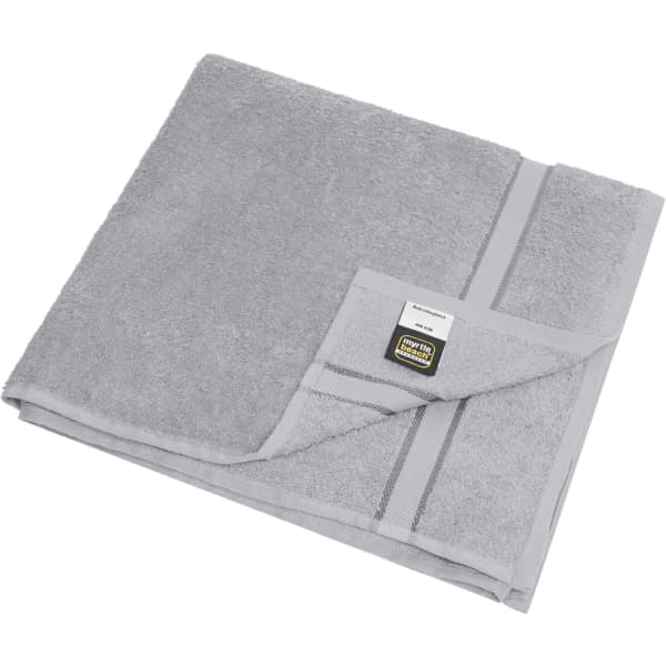 A grey bath towel laid flat, featuring a folded corner and a label with a logo. Soft texture visible.