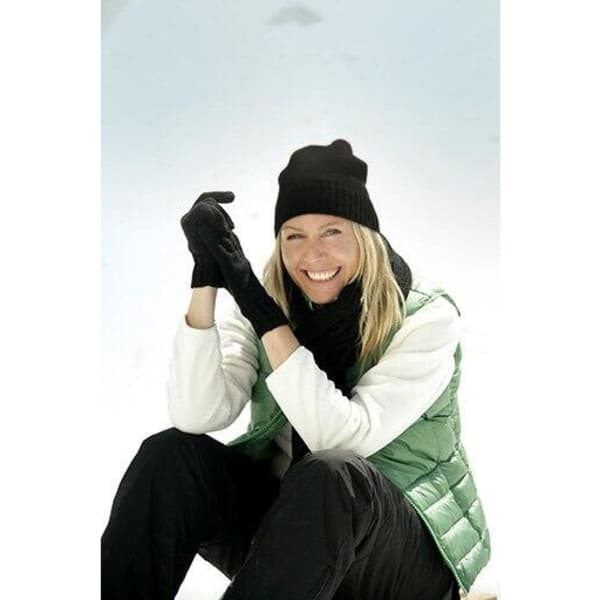 A woman wearing a black beanie and gloves, seated on snow, dressed in a green vest and black pants.