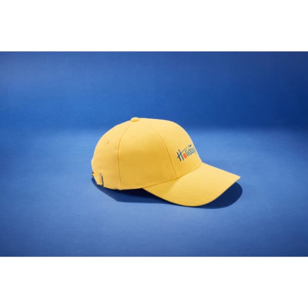 A yellow six-panel cap featuring a logo, displayed against a blue background.