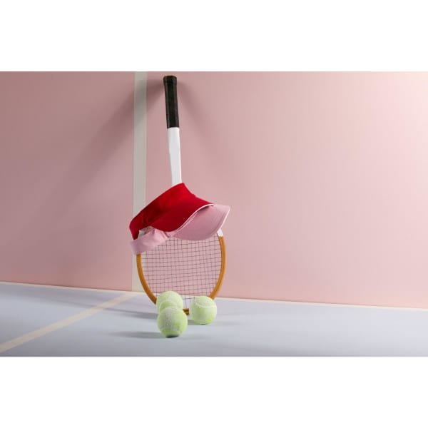 A tennis racket with a red and pink cap rests against it, along with three green tennis balls.
