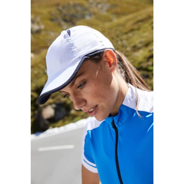 A sports cap in white and navy worn by a woman in a blue cycling outfit, set against a natural background.