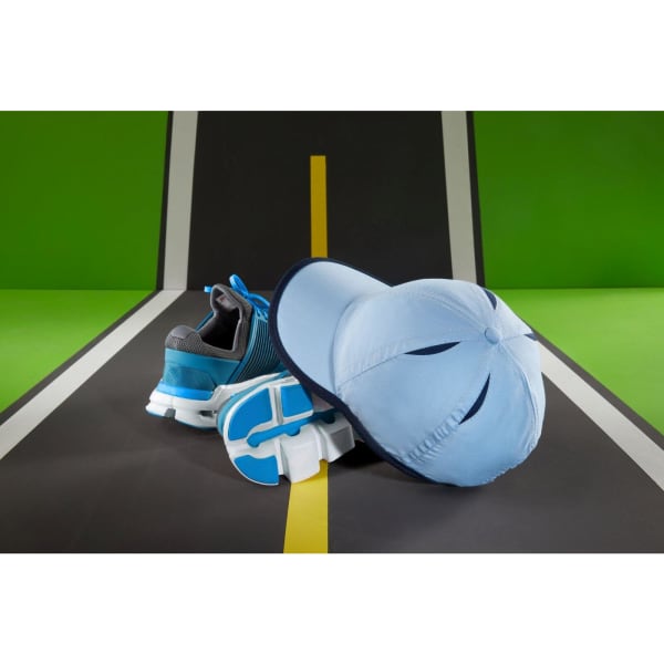 A light blue micro-edge sports cap rests on a surface beside a grey and blue running shoe.