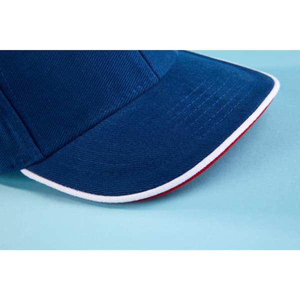 A blue cap with a red underside and a white trim on the brim, featuring a logo.