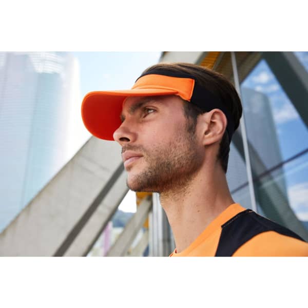 A sport sunvisor in bright orange worn by a man, with a modern urban backdrop. The product features a logo.