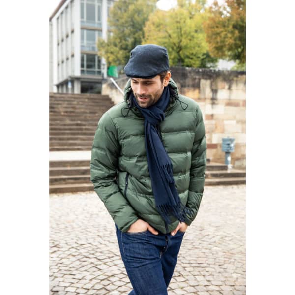 A man wearing a green puffer jacket, a grey cap, and a dark scarf, walking down stone steps in an outdoor setting.
