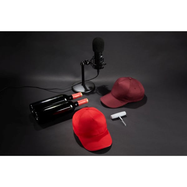 A red cap and a maroon cap are displayed alongside two wine bottles and a microphone, set against a dark background.
