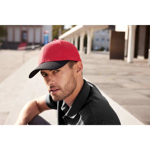 A red and black 6-panel mesh cap featured on a man, set against an outdoor background. The cap has a logo.