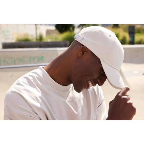 A white 6-panel cap made from bio cotton, worn by a smiling person in a casual setting.