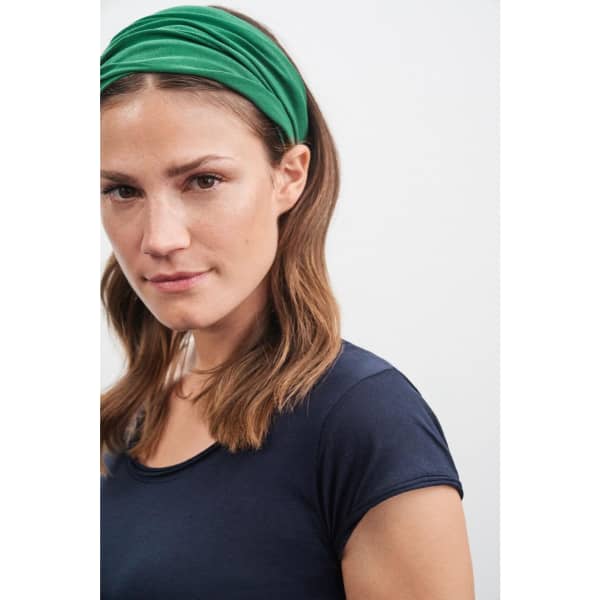 A woman wearing a green bandanna headband, styled with loose waves, against a neutral background.