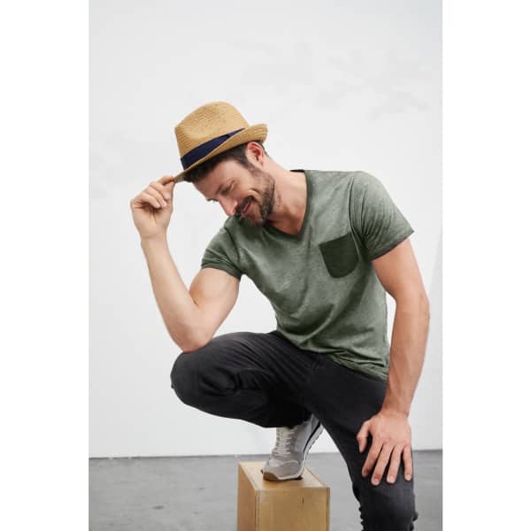 A man wearing a straw Urban Hat with a navy band, styled with a green T-shirt and black trousers.