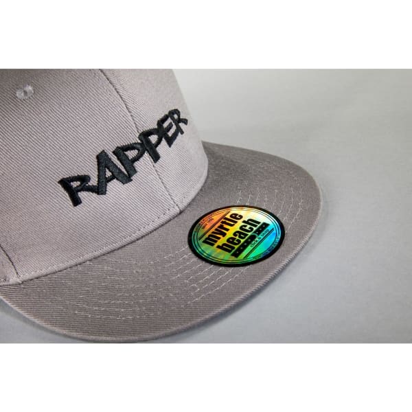 A grey cap featuring "RAPPER" embroidered on the front and a branded sticker on the peak.