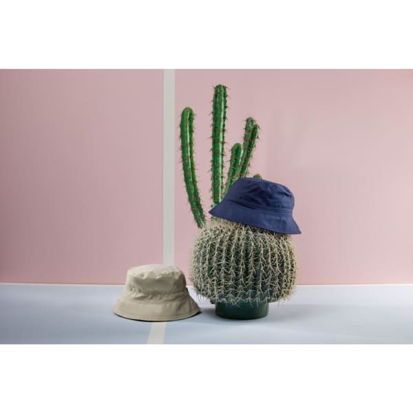 A beige bucket hat and a navy bucket hat placed on a decorative cactus against a pink background.