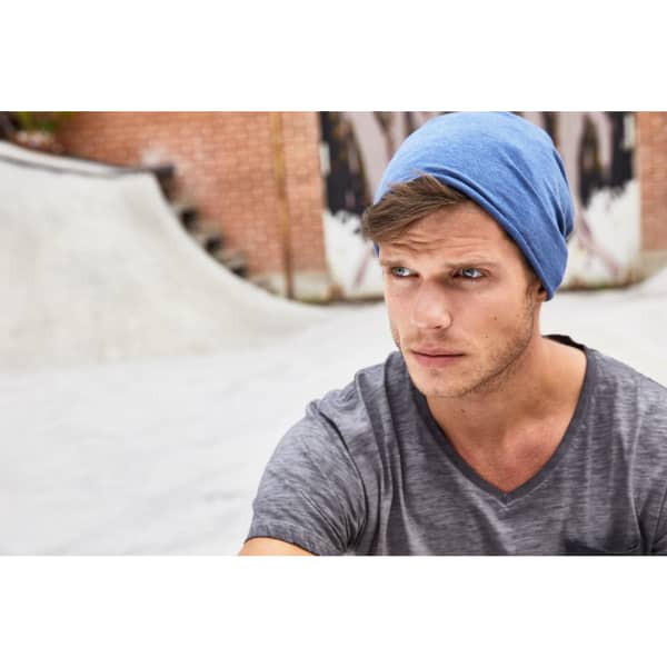 A blue beanie worn by a man, set against an urban background with a textured surface.