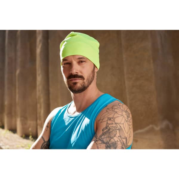 A running beanie in bright fluorescent yellow worn by a man with tattoos, dressed in a blue tank top.