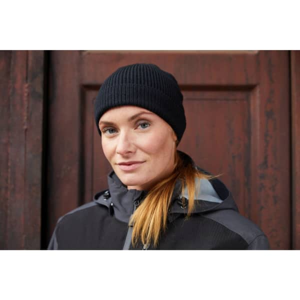 A black ribbed beanie worn by a woman, paired with a dark-coloured jacket against a wooden background.