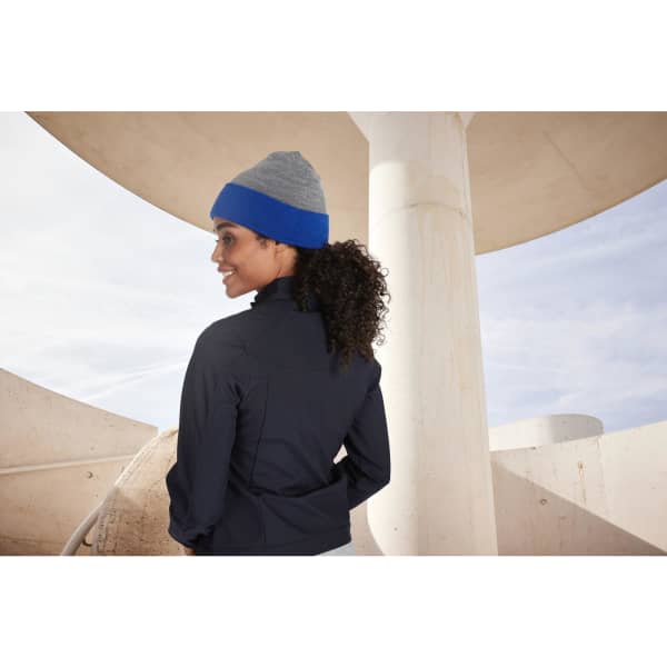 A reversible beanie in grey and blue, worn by a person with curly hair, standing outdoors near architectural features.