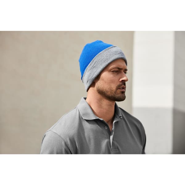 A reversible beanie featuring blue and grey colours, worn by a man in a grey polo shirt.