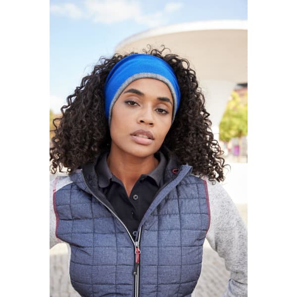 A reversible headband in blue worn by a woman with curly hair, set against an outdoor background.
