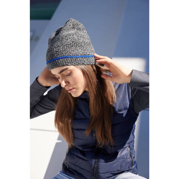 A grey coarse knitted beanie with a blue accent, worn by a woman with long hair in a casual setting.