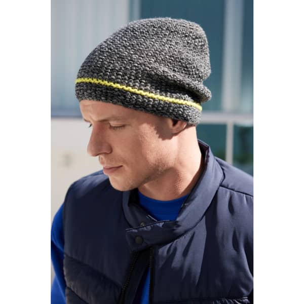 A coarse knitted beanie in grey with a yellow stripe, worn by a man in a navy vest.