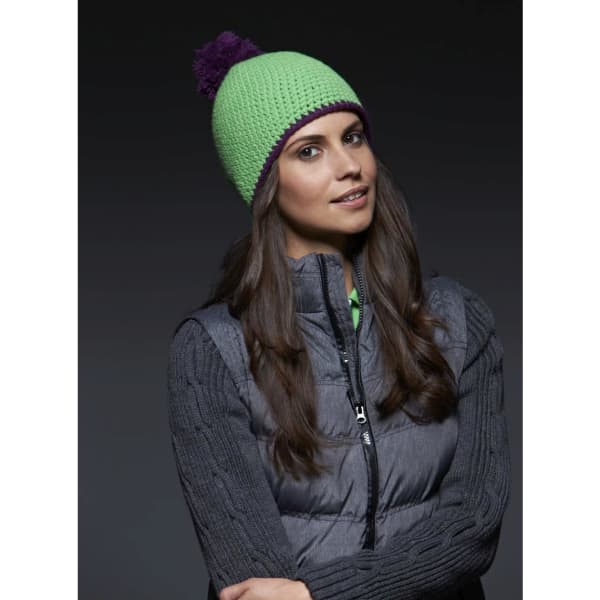 A green knitted hat with a purple pompon, worn by a woman with long hair, paired with a grey vest.