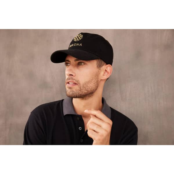 A black 5 panel cap worn by a man, featuring a front logo. He is dressed in a dark polo shirt with grey accents.