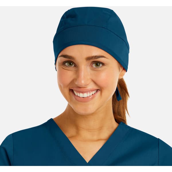 A unisex scrub cap in navy blue, worn by a smiling woman with a ponytail, featuring a logo.