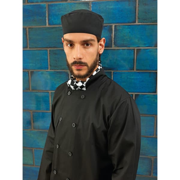 A black chef's skull cap worn by a model, featuring a patterned neck scarf, set against a blue tiled background.