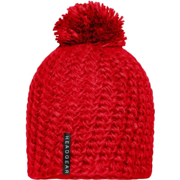 A red crocheted cap with a large pompon on top and a branding label.