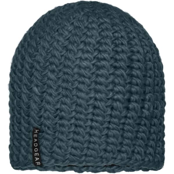 A crocheted beanie in a deep teal colour, featuring a branding label on the side.